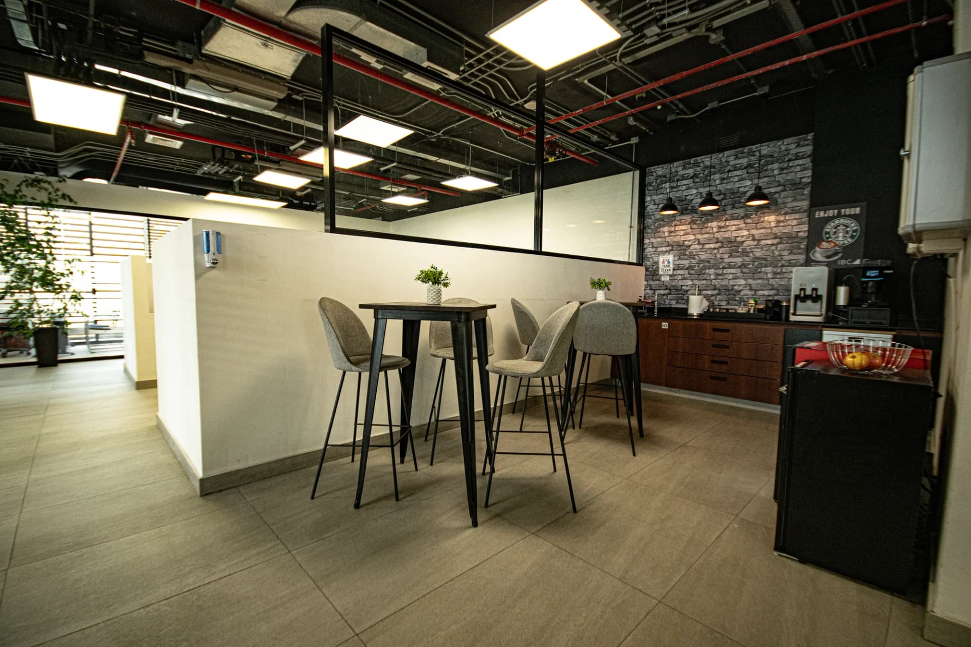 Cafetería con mesa alta, muro de ladrillo y máquina de café